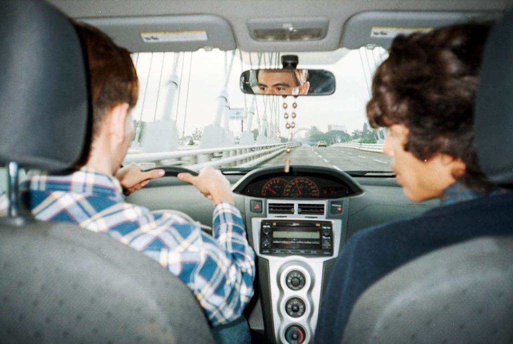 a-man-driving-a-car-with-another-man-in-the-back-seat-otcwqtlfjmq