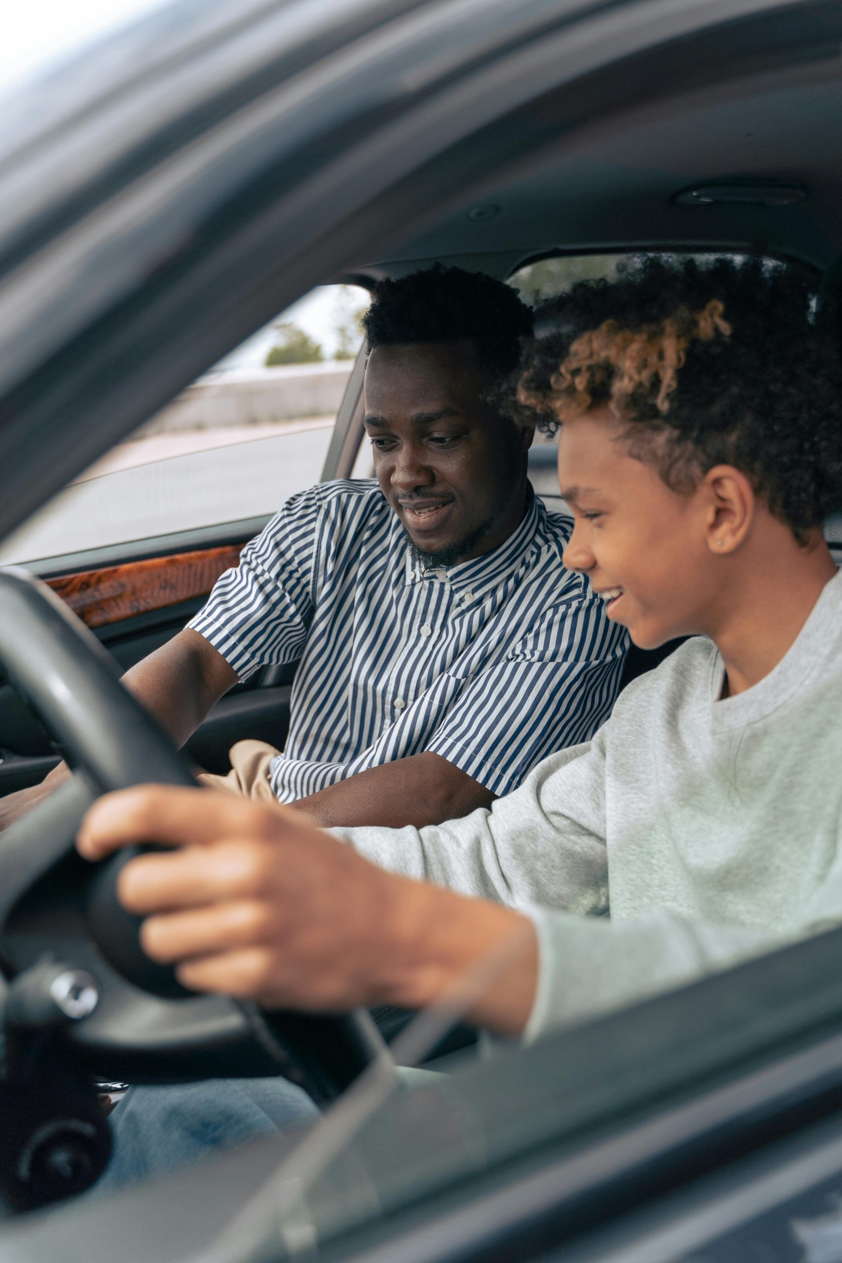 Father and teenage son sitting in a car, bonding while learning to drive.